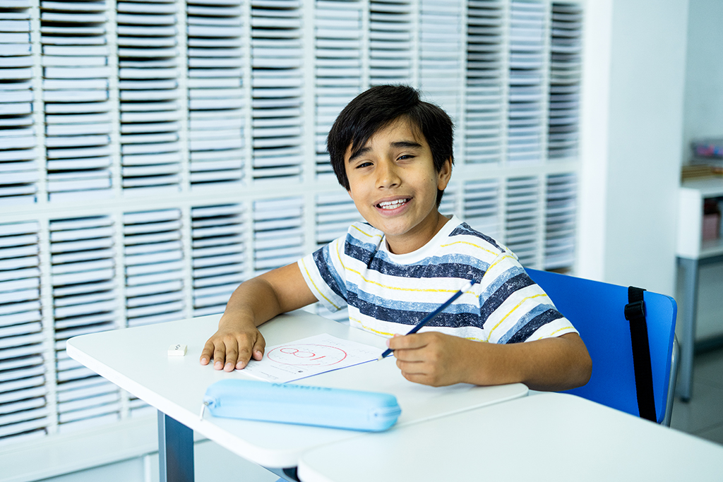 Alumno sentado, sosteniendo un lápiz y sonriendo en el aula de un centro Kumon-Bolivia